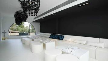 Un interior moderno con un sofá blanco largo, varias mesas redondas blancas y una lámpara de araña negra original.