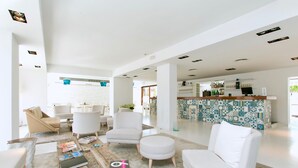 A modern hotel lobby with white furniture, a coffee table with magazines, and a tiled bar area.