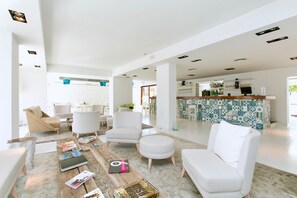 Un hall d’hôtel moderne, avec des meubles blancs, une table basse sur laquelle sont posés des magazines et un bar carrelé.