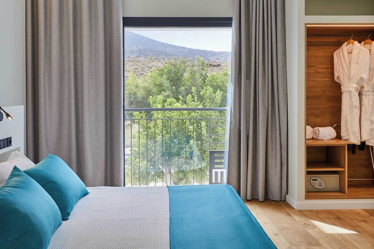 Une chambre à coucher comprenant un lit, une armoire et un balcon avec vue sur les arbres et les collines.