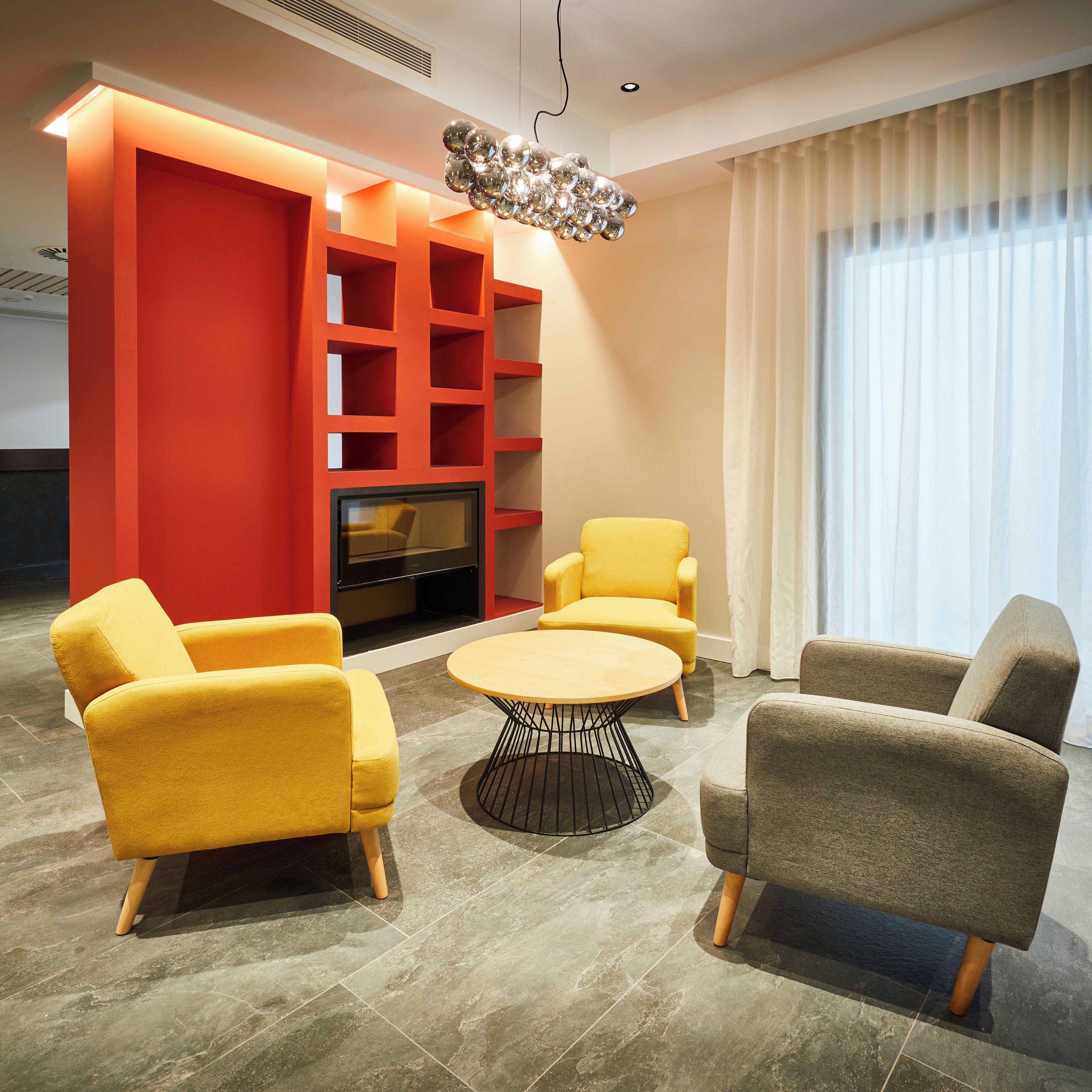 Una sala moderna con una pared de acento roja, un televisor y dos sillones amarillos.