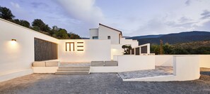 Ein modernes architektonisches Design mit weißer Fassade, einer Treppe, die zu einem ebenerdigen Eingang führt, und Blick auf die umliegende Landschaft.