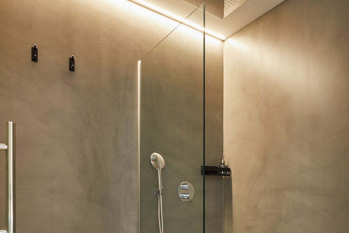A modern shower with a glass door, a handheld showerhead, and a towel on the floor.