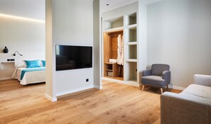 A modern living room with a flat-screen TV mounted on the wall, a wooden wardrobe with a mirror, and a grey armchair. - Hotel Boutique Molino De Enmedio (Hueneja)