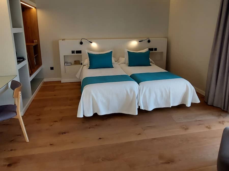 A bedroom with two beds, a desk, and a shelving unit.