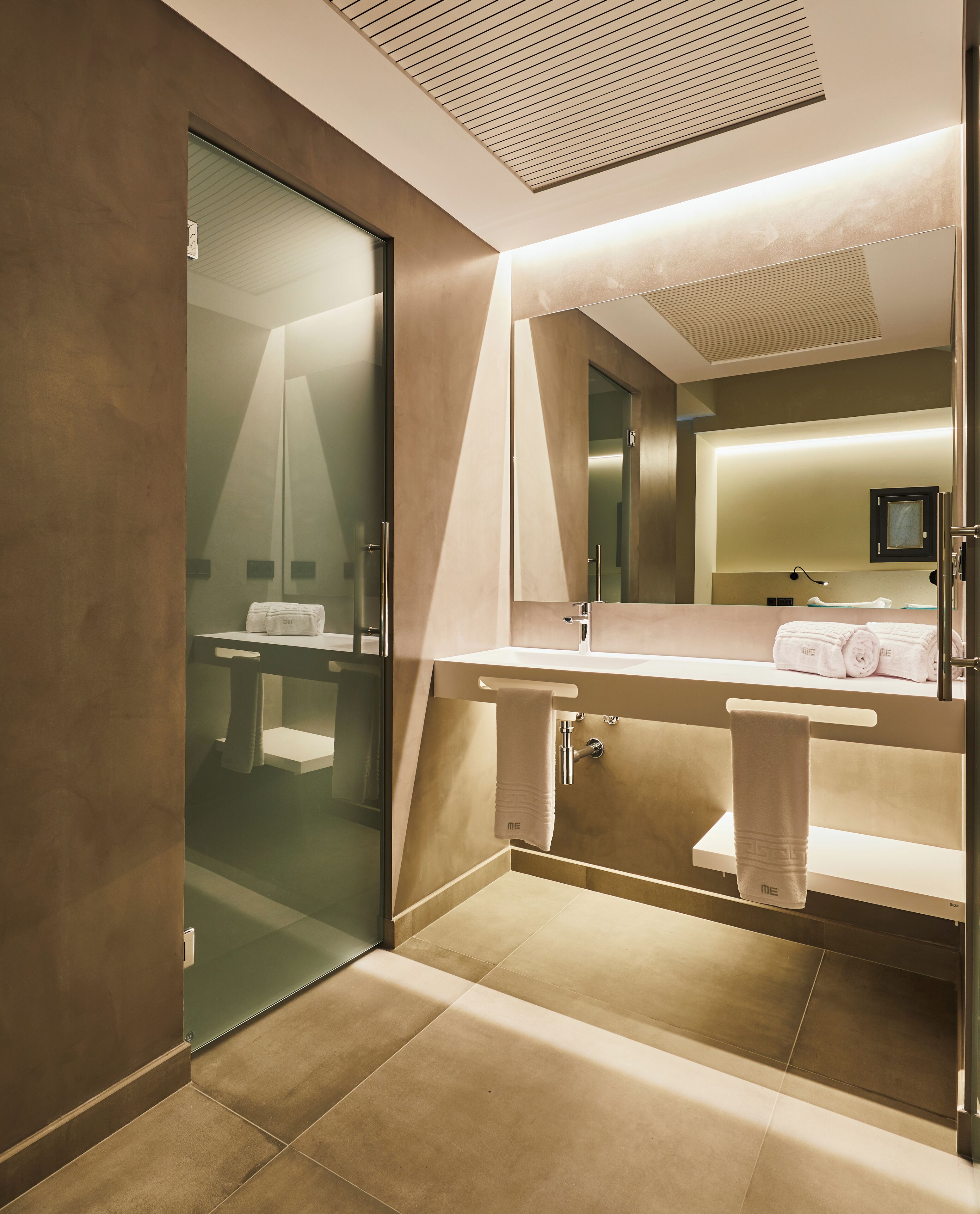 Une salle de bain moderne dotée d’une douche à parois de verre, d’un grand miroir et d’un meuble-lavabo avec un porte-serviettes.