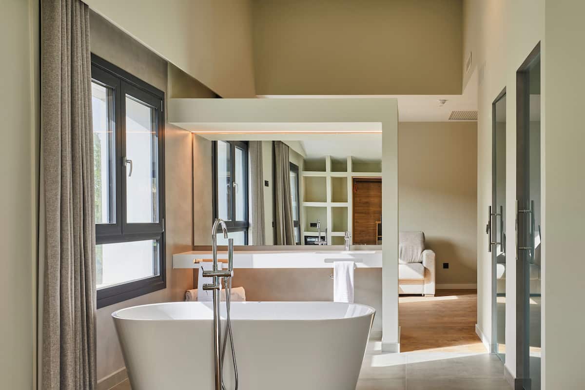 A modern bathroom with a freestanding bathtub, a large mirror, and a wooden floor.