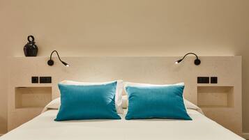 A neatly made bed with two blue pillows and a white bedspread. There are two wall-mounted light fixtures on either side of the bed.