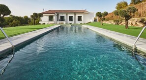 A rectangular swimming pool with clear blue water, surrounded by a well-maintained lawn and a white building with a tiled roof in the background. - Hotel Boutique Molino De Enmedio (Hueneja)
