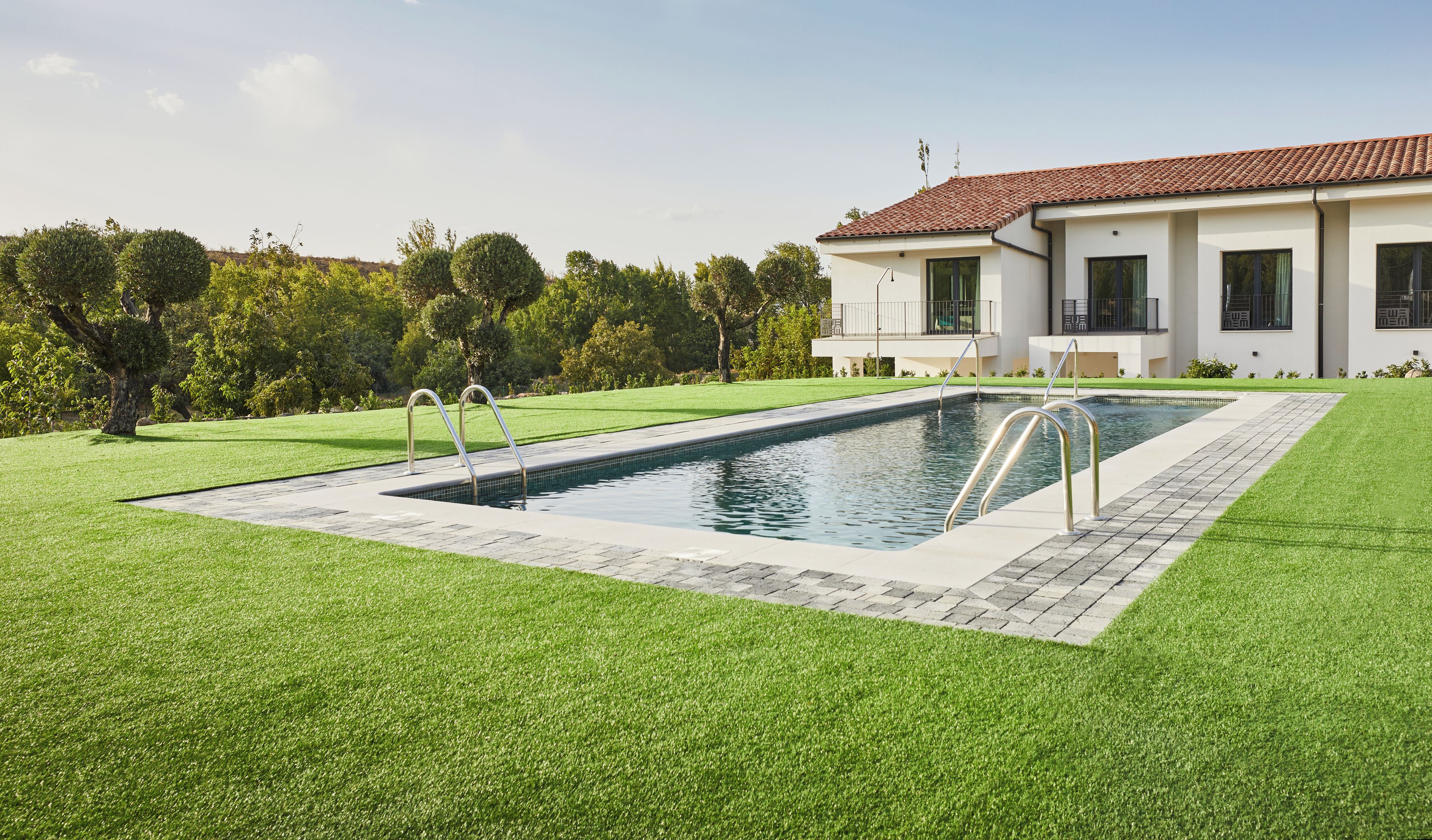 A modern house with a swimming pool, surrounded by well-maintained lawn and trees.