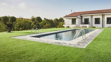 A modern house with a swimming pool, surrounded by well-maintained lawn and trees.