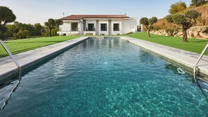 A rectangular swimming pool with clear blue water, surrounded by a well-maintained lawn and a white building with a tiled roof in the background. - Hotel Boutique Molino De Enmedio (Hueneja)