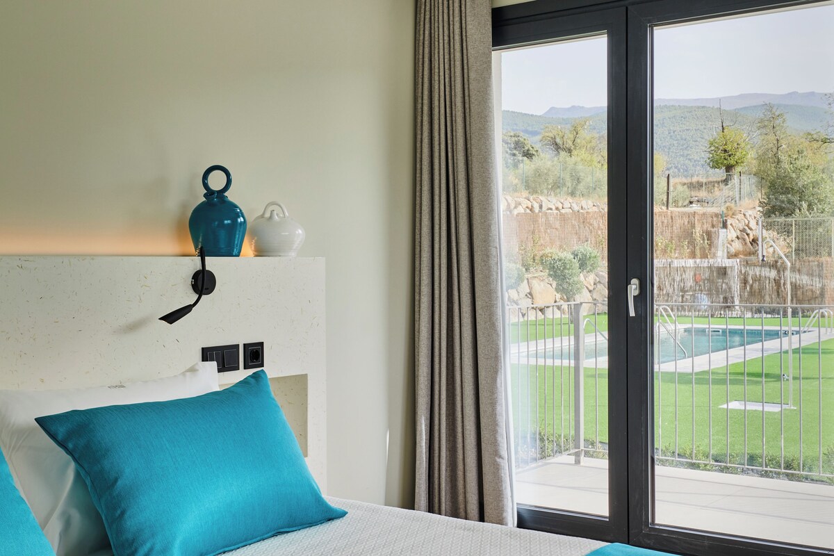 A hotel room with a large bed, a view of a pool and mountains, and a window with curtains.
