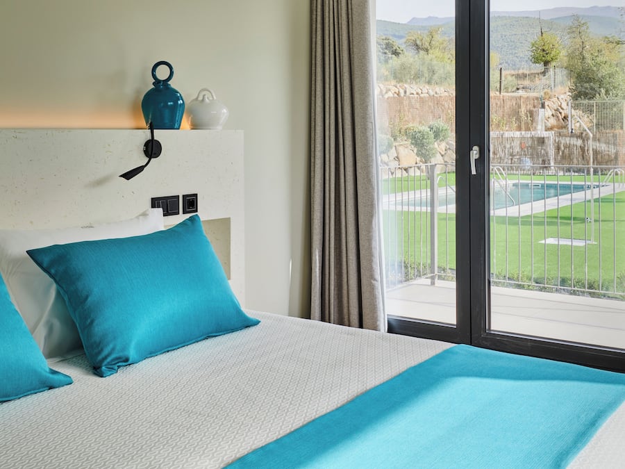 A hotel room with a large bed, a view of a pool and mountains, and a window with curtains.