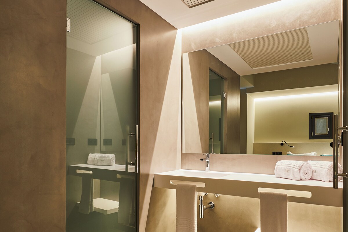 A modern bathroom with a glass shower enclosure, a large mirror, and a vanity with a towel rack.