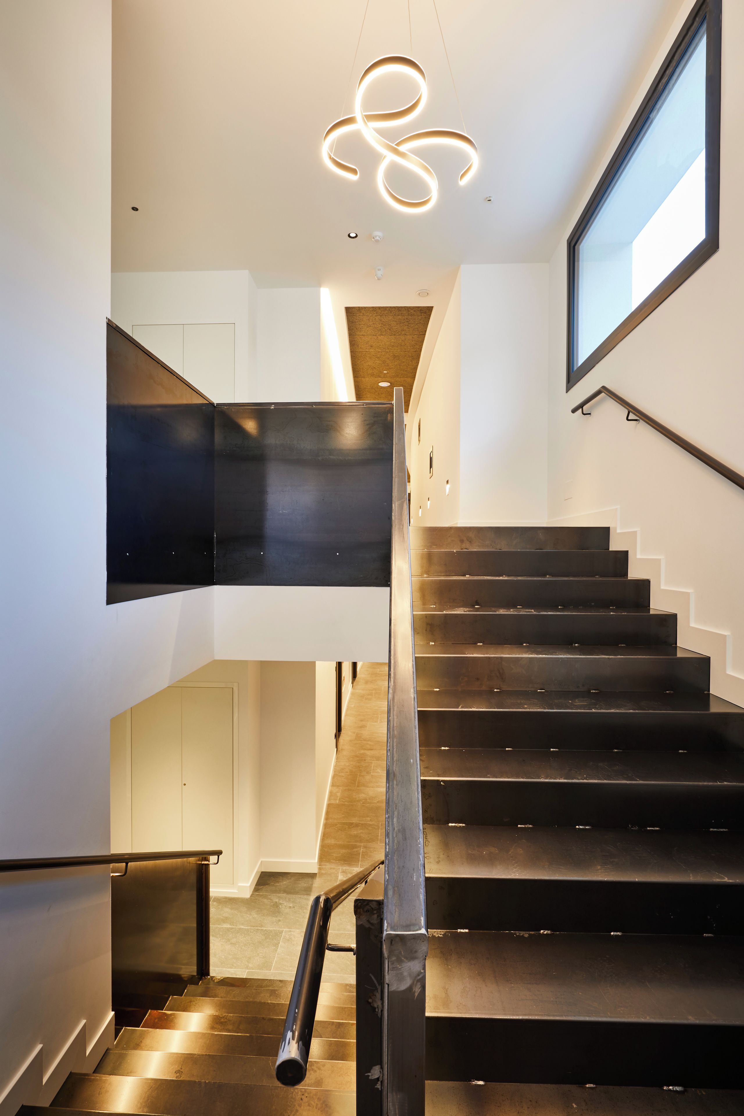 A modern staircase with a metal railing, a wall-mounted light fixture, and a large window on the right.