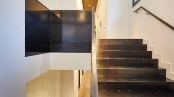 A modern staircase with a metal railing, a wall-mounted light fixture, and a large window on the right.