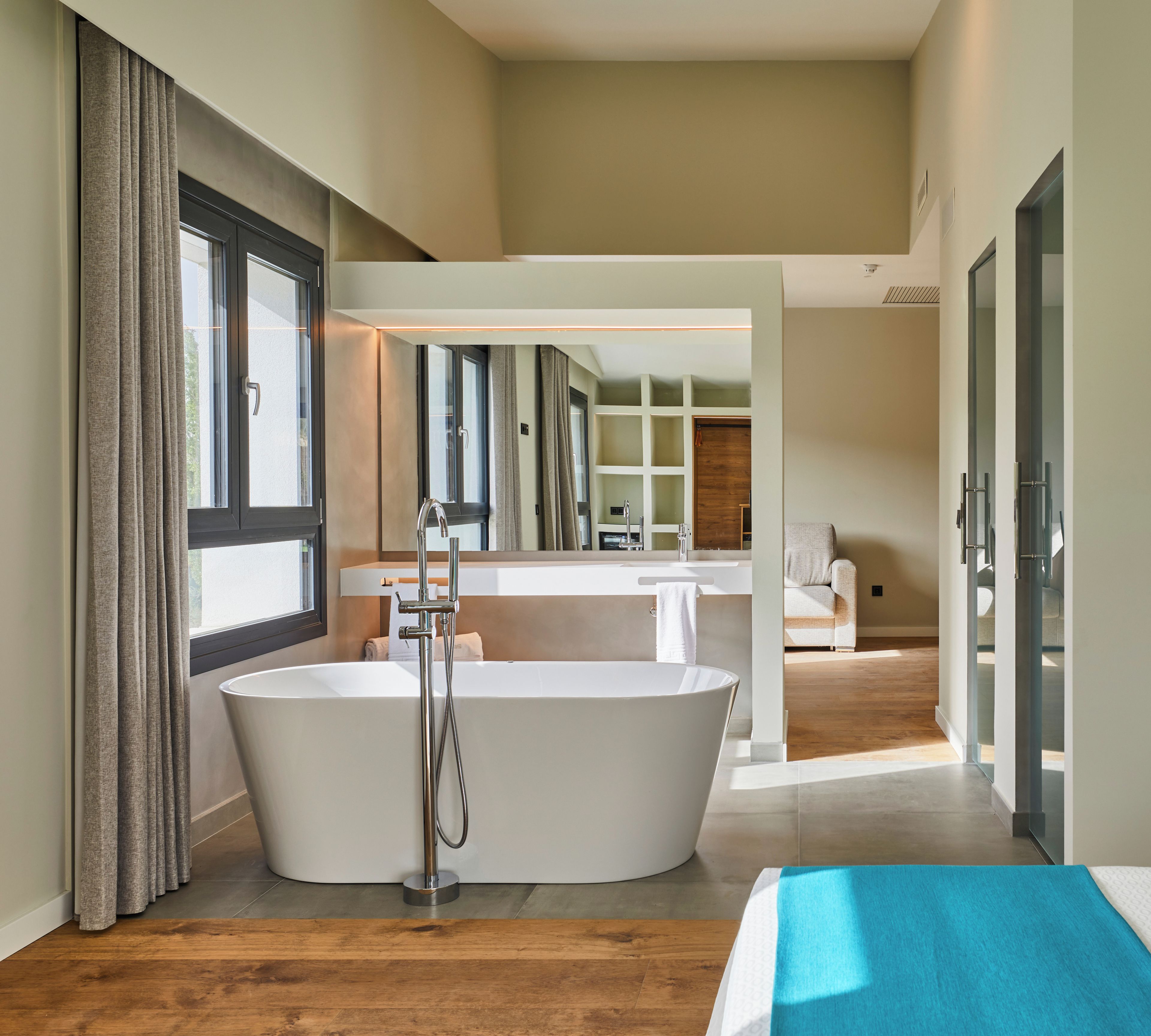 Un baño moderno con una bañera independiente, un espejo grande y suelo de madera.