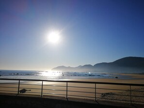 A beach with a metal railing in the foreground, a clear sky, and distant mountains. - Apartamentos Gran Socaire De Noja (Noja)