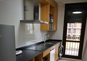 A compact kitchen with a black countertop, stainless steel sink, and wooden cabinets. - Apartamentos Gran Socaire De Noja (Noja)