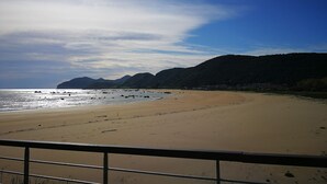 Een strand met een heldere lucht, bergen op de achtergrond en een hekwerk in de voorgrond.