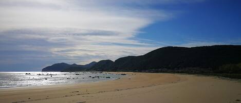 Ein Strand mit blauem Himmel, Bergen im Hintergrund und einem Geländer im Vordergrund.