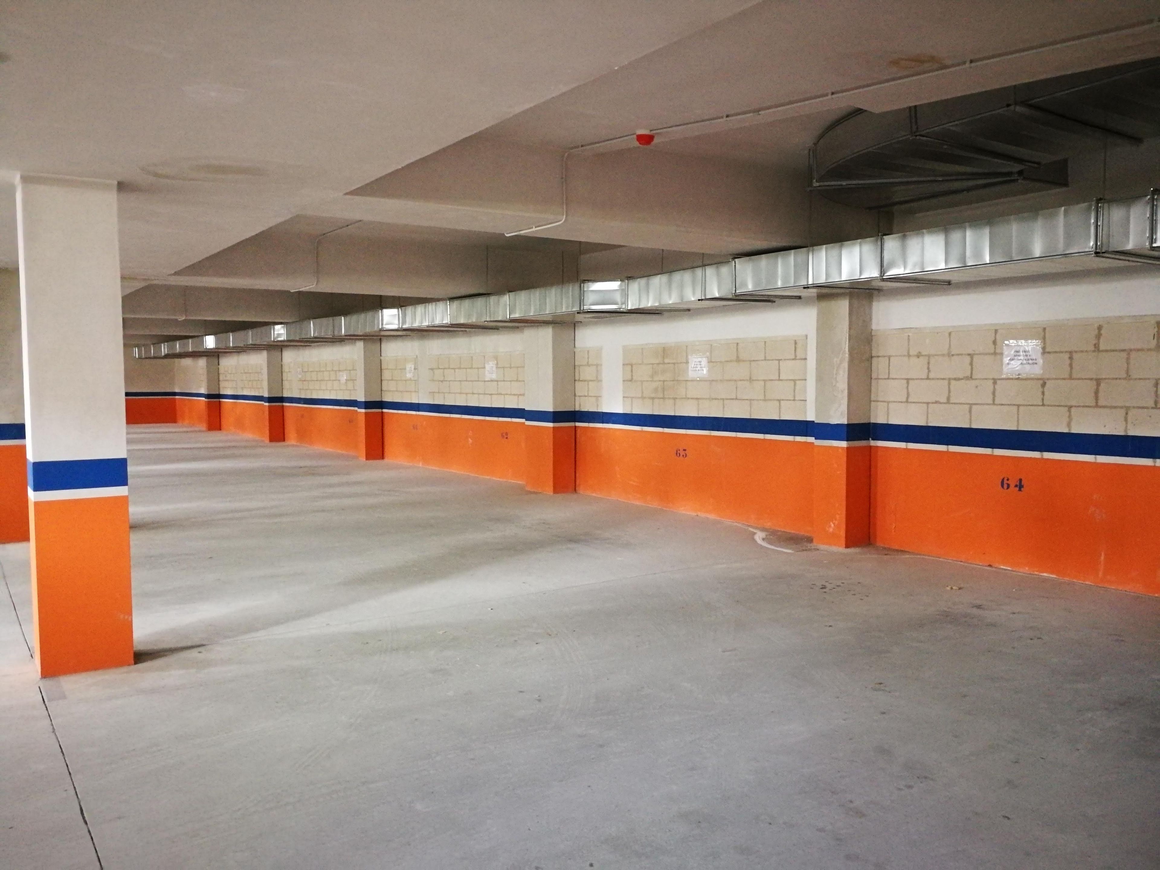 A parking garage with multiple parking spaces, concrete floors, and walls painted in orange and blue.
