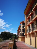 A multi-story building with balconies, a paved walkway, and a clear blue sky.