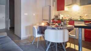 A modern kitchen with red cabinets, a microwave, and a dining area with a table set for two. - Entrevias Lodging (León)