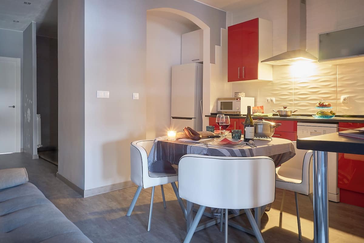 A modern kitchen with red cabinets, a microwave, and a dining area with a table set for two.