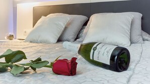 A neatly made bed with pillows, a bottle of wine, and a rose on a white textured bedspread. - Entrevias Lodging (León)