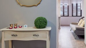 A modern living room with a grey wall, a white console table with drawers, a green spherical decoration, and a grey sofa with patterned cushions. - Entrevias Lodging (León)