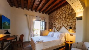 A bedroom with a bed, a desk, a chair, a stone wall, and a window with curtains. - Abba Las Viñas Tiedra Hotel Rural (Tiedra)