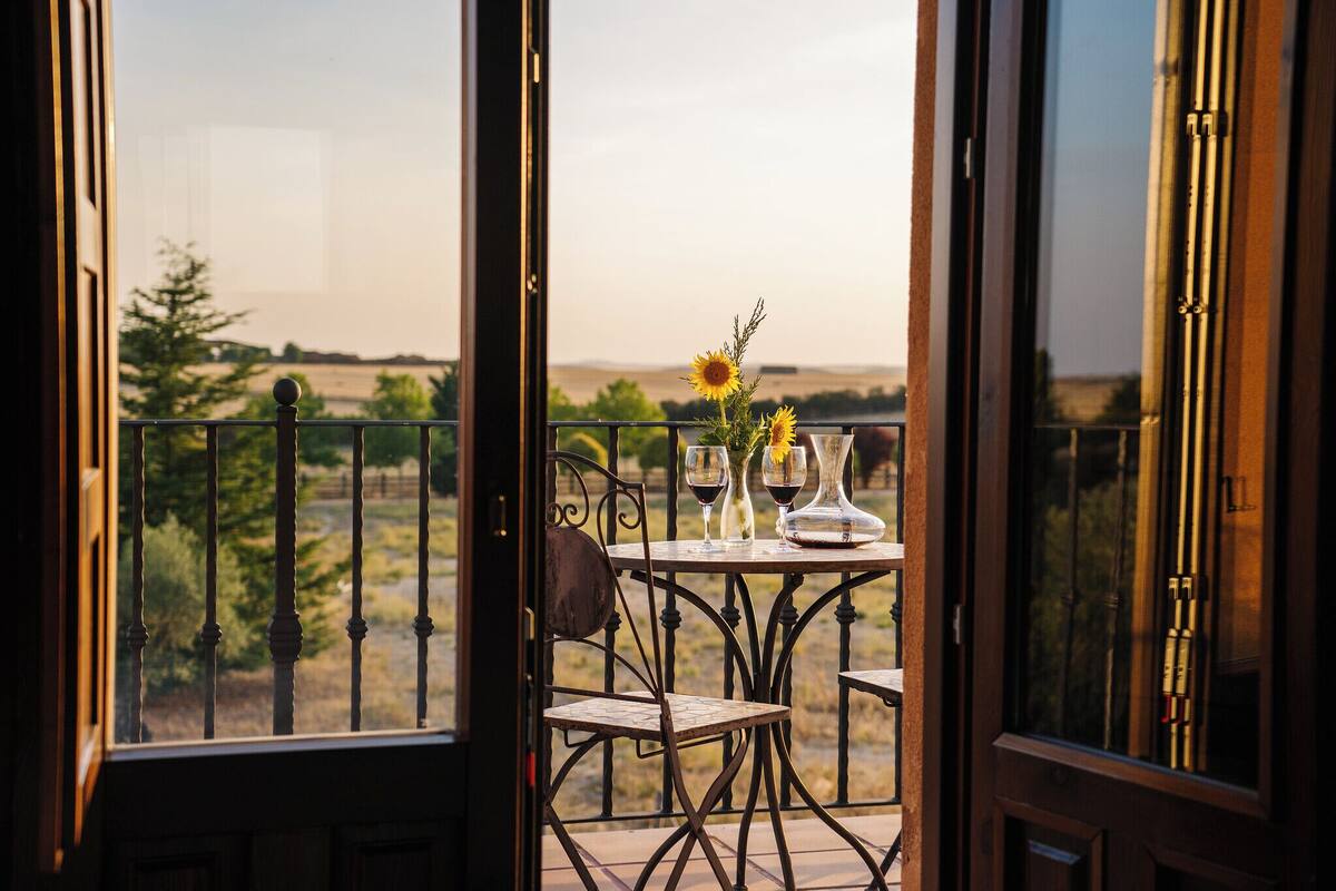 Un balcon avec une table dressée pour deux personnes, agrémenté d’un vase rempli de tournesols et de deux verres à vin.