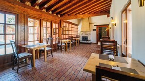 A rustic dining area with wooden tables and chairs, brick flooring, and exposed wooden beams.