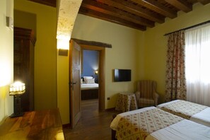 A hotel room with a wooden ceiling, a bed with floral bedding, a chair, a small table, and a television on the wall. - Abba Las Viñas Tiedra Hotel Rural (Tiedra)