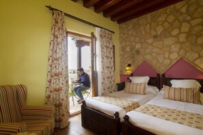 A hotel room with two beds, a chair, and a view of the outdoors.