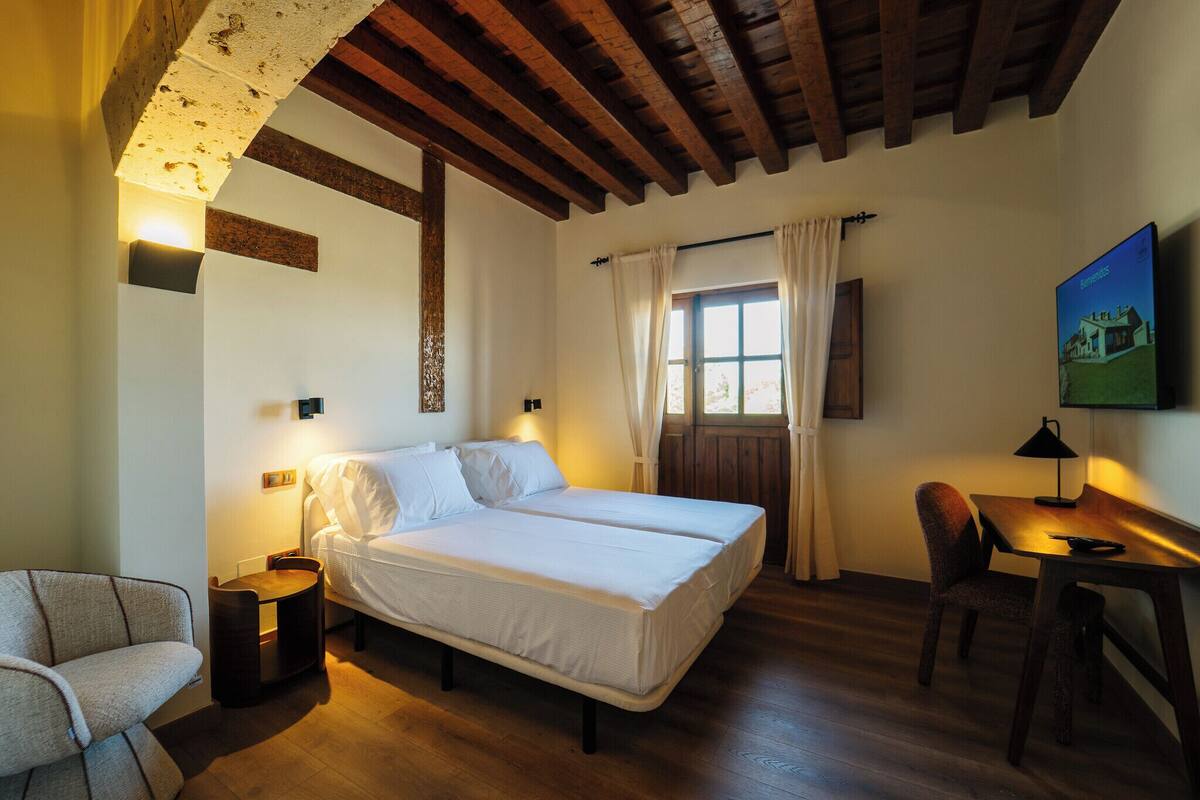 Une chambre à coucher avec un lit, une chaise, un bureau et une fenêtre avec des rideaux.