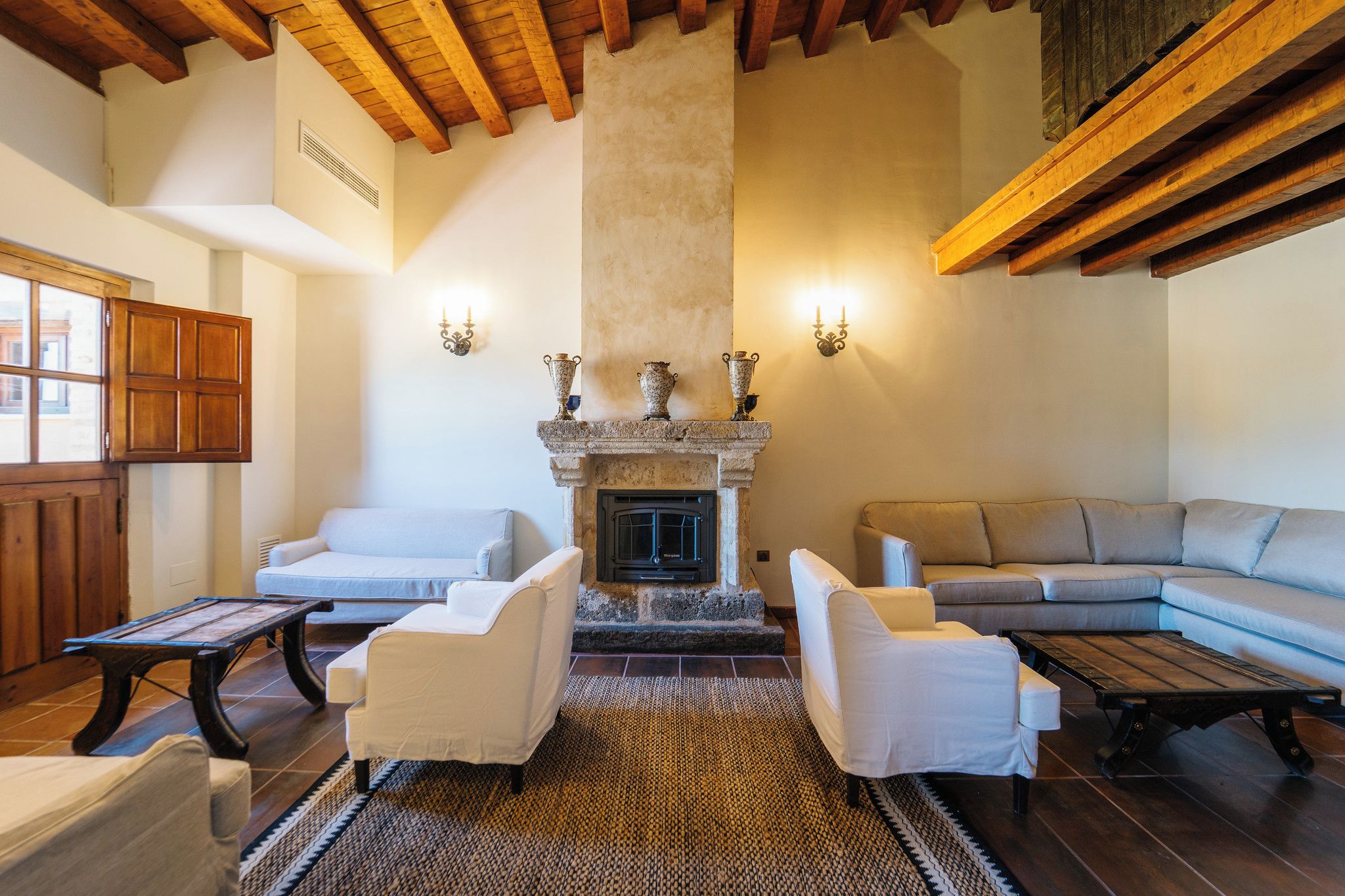 A cozy living room with a fireplace, white sofas, and wooden beams on the ceiling.