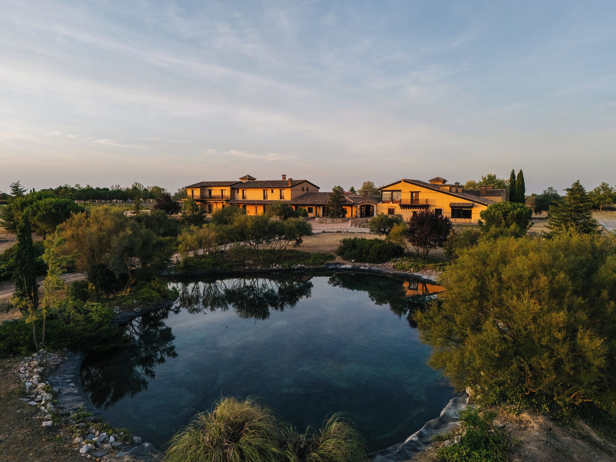 A large house with multiple buildings, a pond, and surrounding greenery.