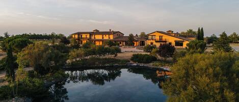 A large house with multiple buildings, a pond, and surrounding greenery.