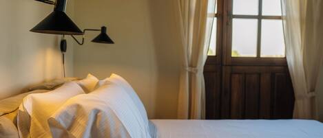 A neatly made bed with white linens, a black wall-mounted lamp, and a window with curtains.
