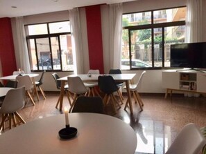 Un comedor con mesas y sillas, ventanas amplias y un televisor.