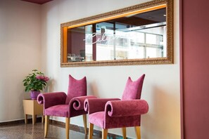 Una habitación con dos sillones suaves color rosa, una mesita auxiliar con una planta en maceta y un espejo grande con marco dorado.