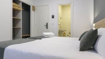 Quarto de hotel com cama grande, guarda-roupa e casa de banho visível através de uma porta aberta.