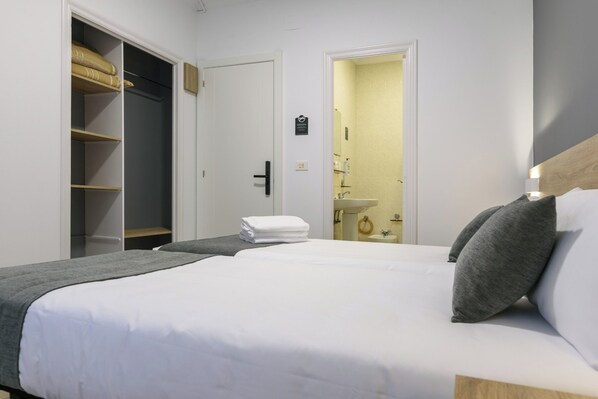 Habitación de hotel con una cama grande, un armario y un baño visible a través de una puerta abierta.