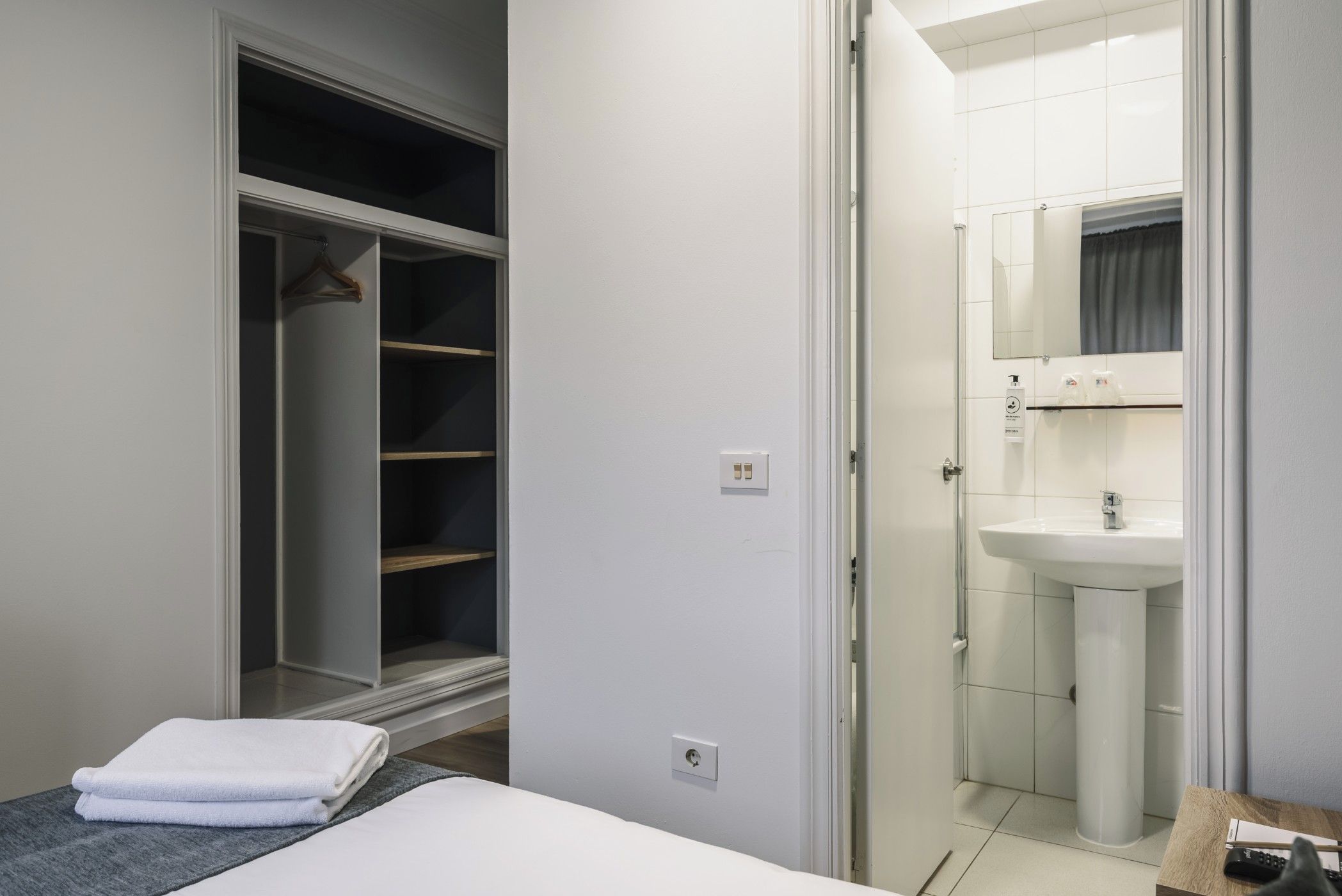 Hotelkamer met een bed, inloopkast en badkamer met wastafel en spiegel.