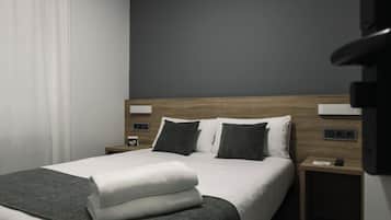 A modern hotel room with a neatly made bed, a wooden headboard, and a nightstand with a phone and a small lamp.