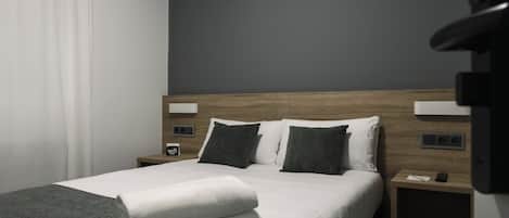 Une chambre d’hôtel moderne avec un lit bien fait, une tête de lit en bois et une table de chevet sur laquelle se trouvent un téléphone et une petite lampe.