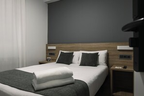 A modern hotel room with a neatly made bed, a wooden headboard, and a nightstand with a phone and a small lamp.